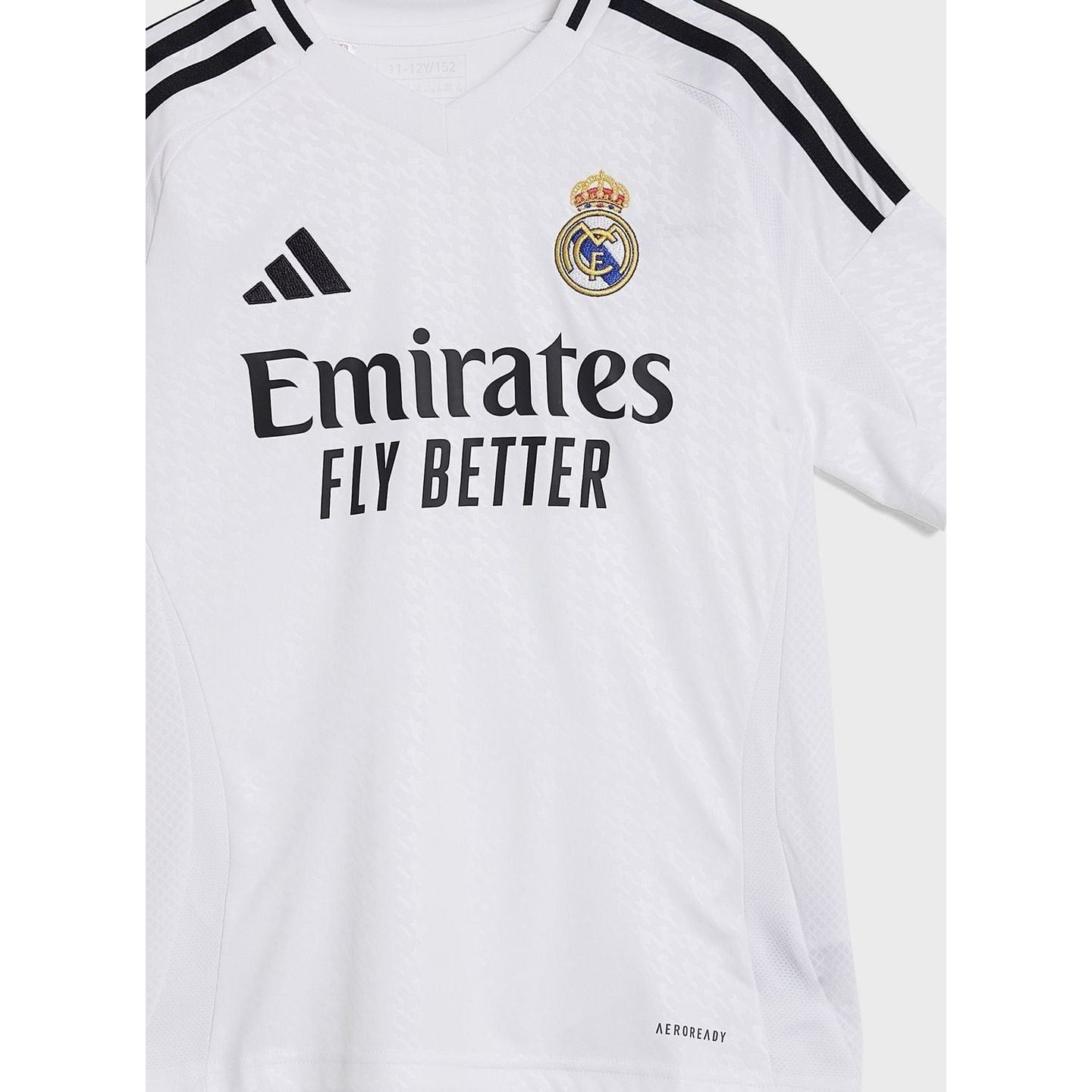 Détail en gros plan de l'écusson du Real Madrid tissé sur la poitrine gauche du maillot junior.