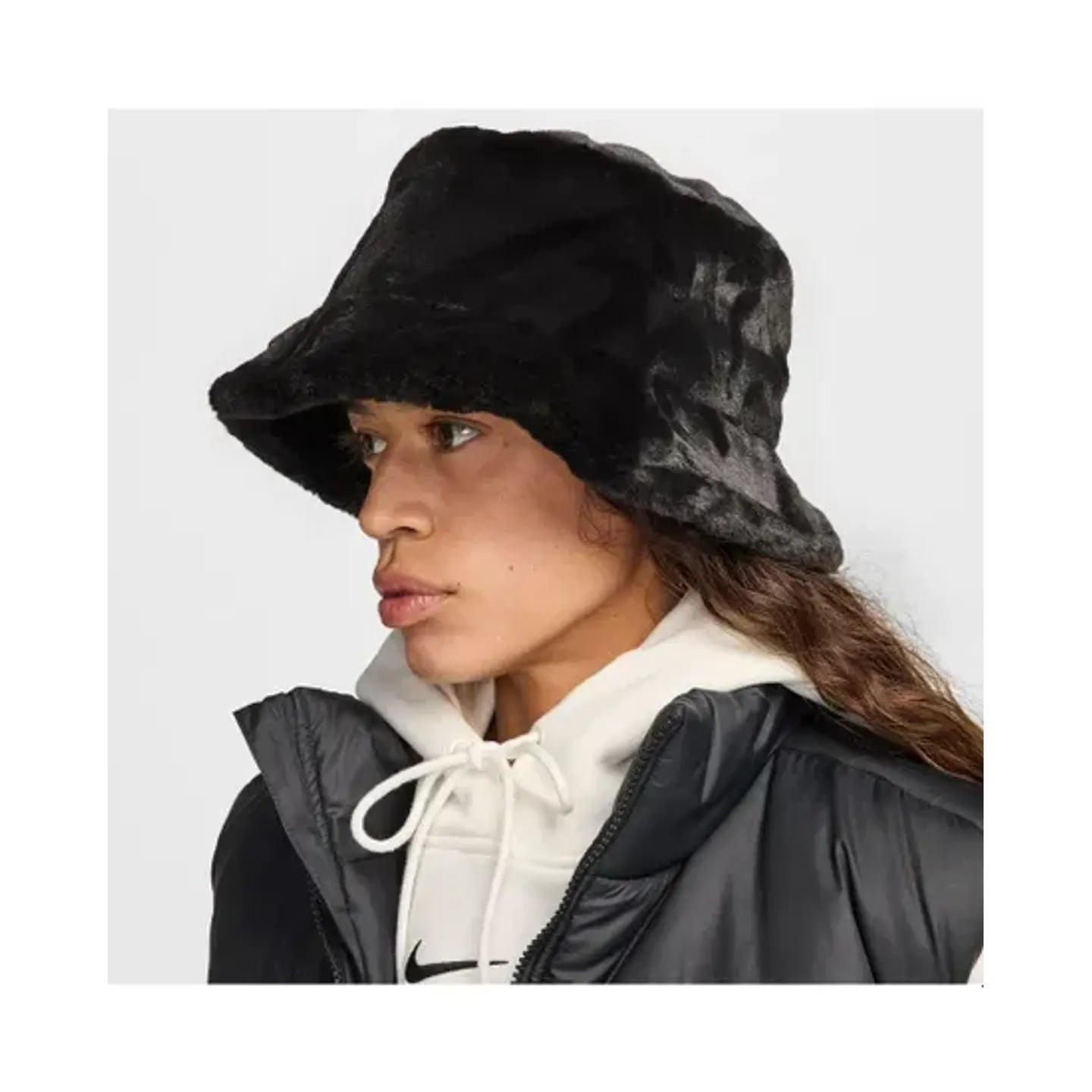 Profil d'un mannequin portant le bob Nike Apex en fausse fourrure noire, sweat à capuche blanc et gi
