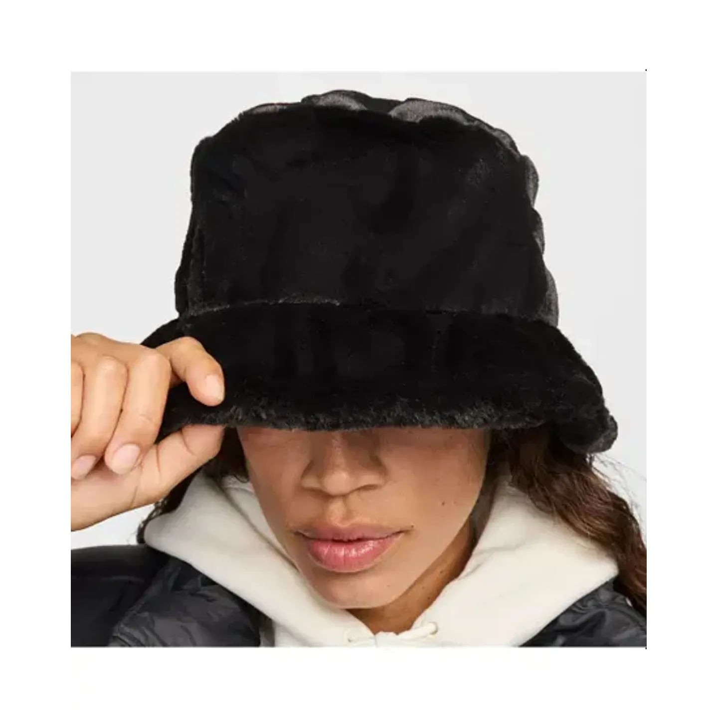 Gros plan d'une main ajustant le bord duveteux du bob en fausse fourrure Nike Apex noir sur un sweat