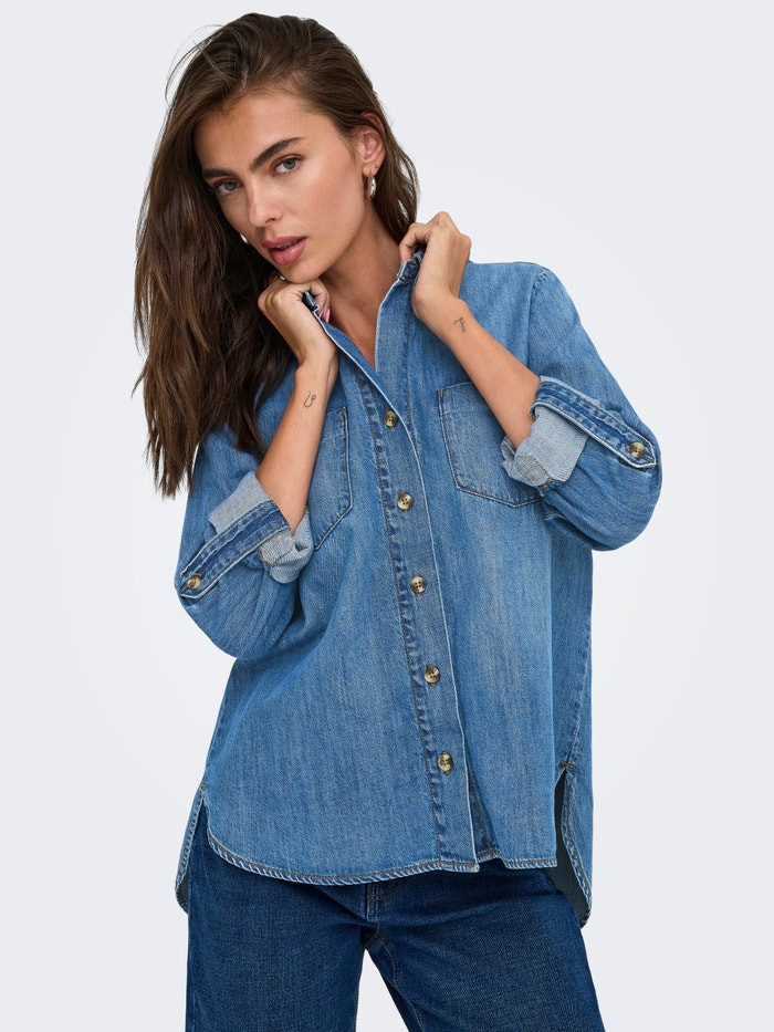 Model holding collar of ONLYASMIN denim shirt with sleeves rolled up over dark blue jeans