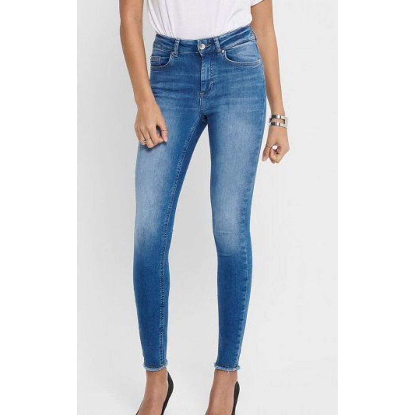 Mannequin portant un jean skinny taille mi-haute ONLY bleu, ourlet brut aux chevilles, haut blanc et