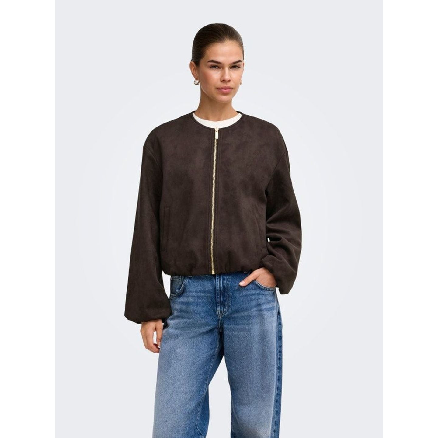 Mannequin portant la veste bomber en simili suède ONLSTINA marron foncé avec un jean bleu, mains dan