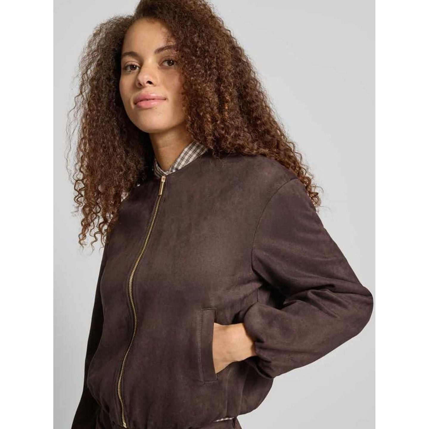 Femme en bomber en faux suède marron foncé sur chemise à carreaux, main dans la poche latérale, vue 