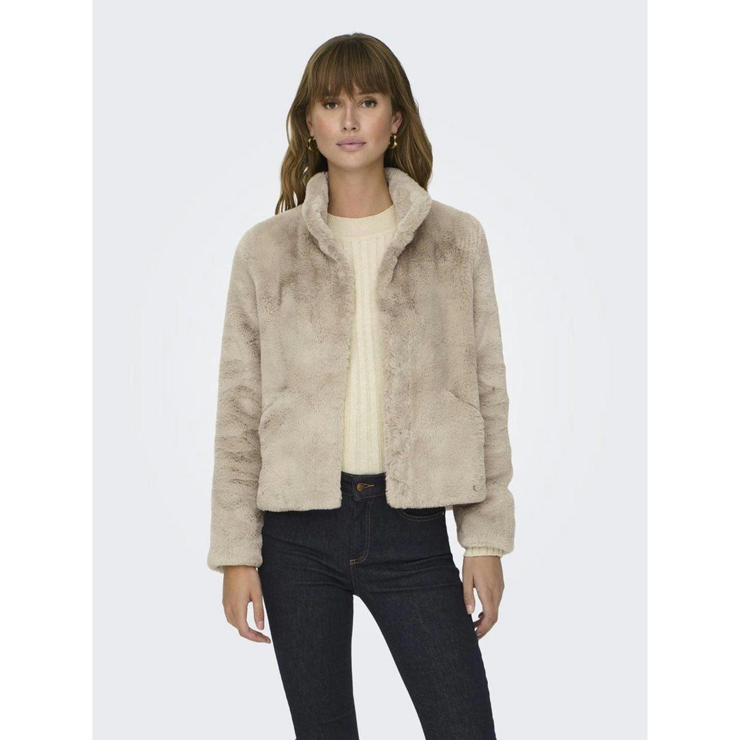 Mannequin portant la veste courte en fausse fourrure beige sur un pull crème et un jean skinny foncé