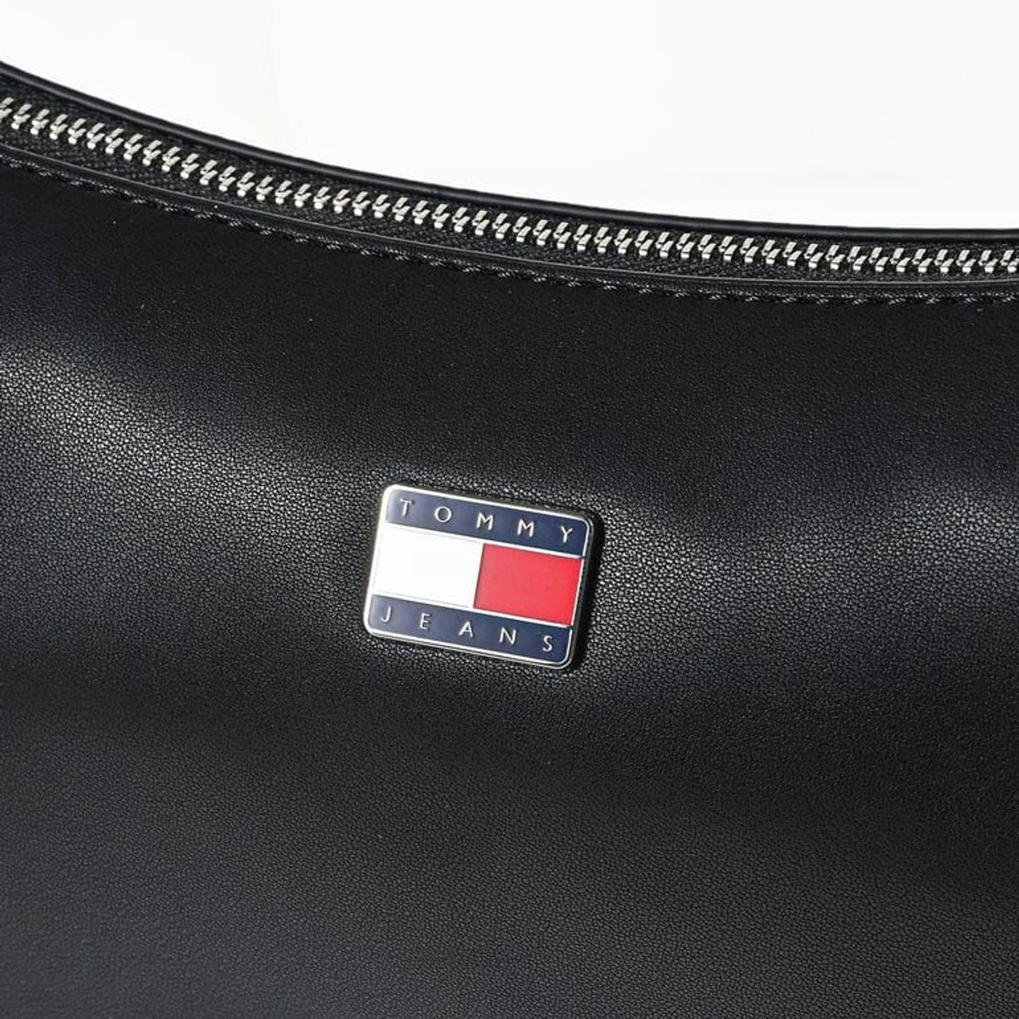 Gros plan macro de l'emblème drapeau métallique Tommy Jeans sur similicuir grainé noir