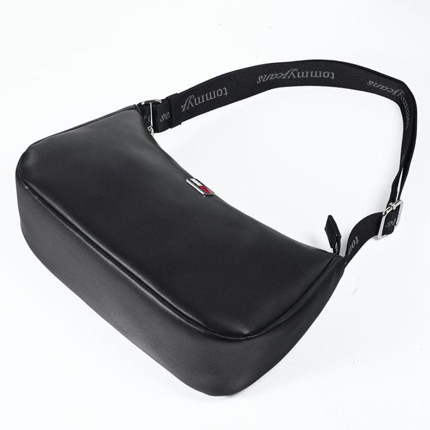 Vue inclinée du sac d'épaule noir montrant la bandoulière en sangle logo Tommy Jeans et les boucles