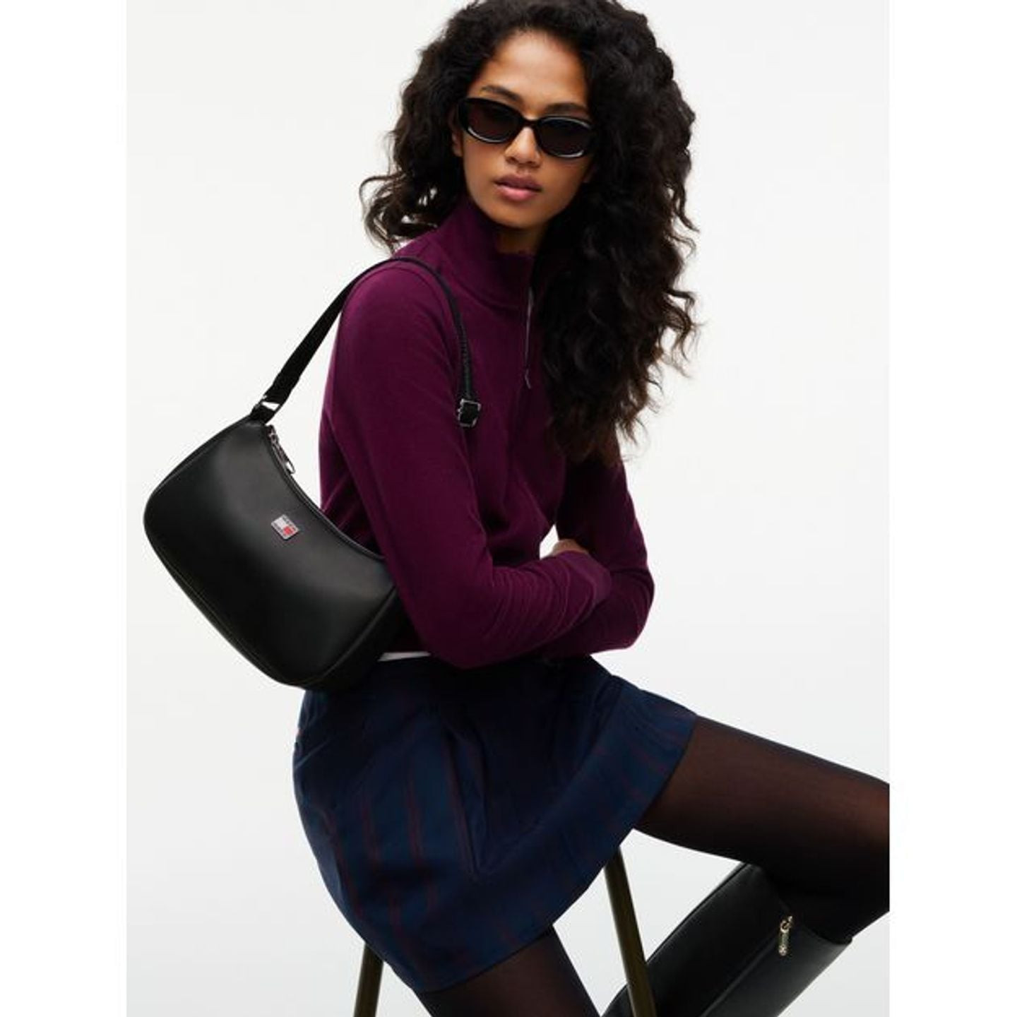 Femme portant un sac d'épaule noir avec col roulé bordeaux et jupe marine en photo lifestyle
