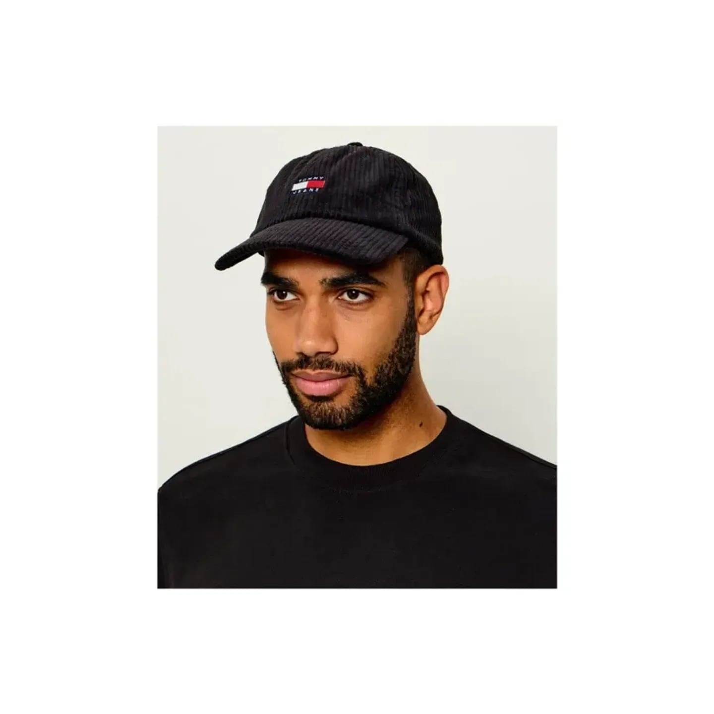 Homme portant la casquette Tommy Jeans Heritage en velours côtelé noir avec un sweat col rond noir.