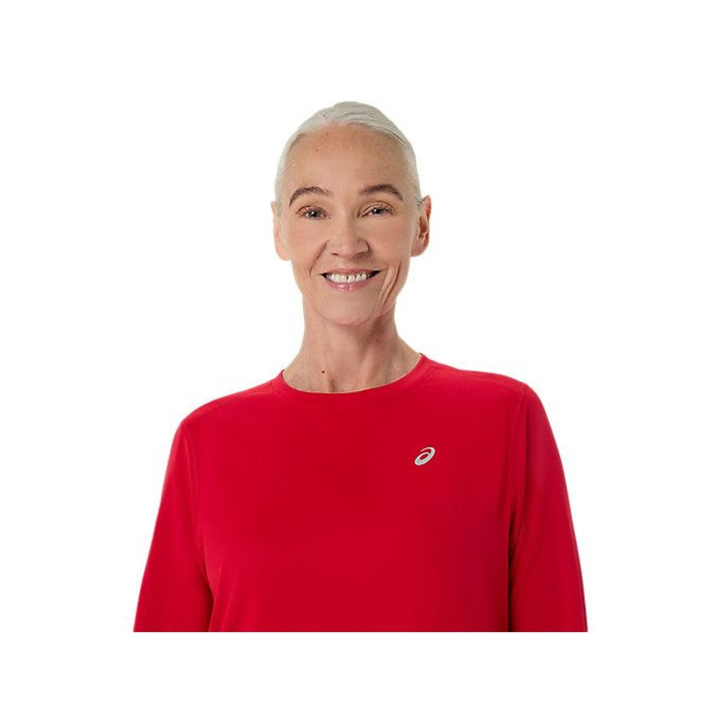 Femme souriante portant le ASICS CORE LS TOP rouge avec un petit logo blanc sur la poitrine