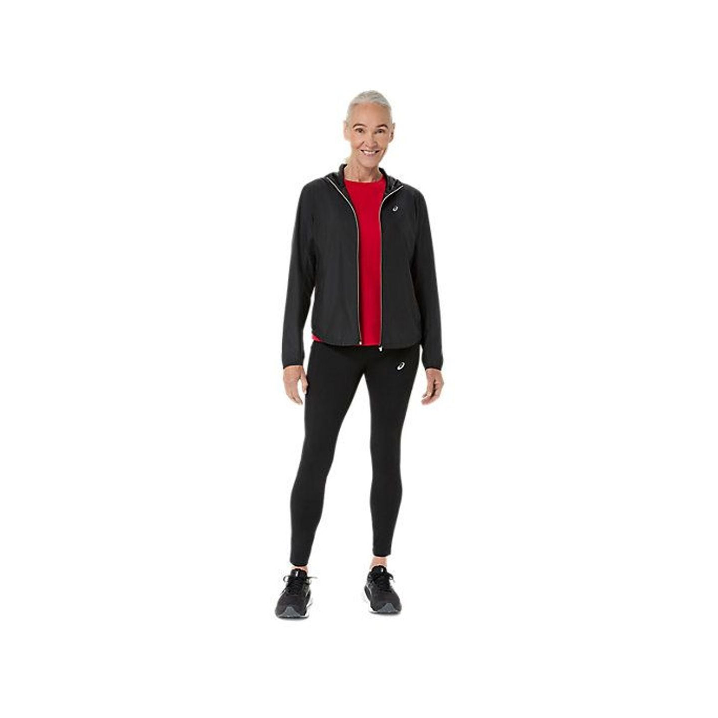 Femme portant le CORE LS TOP ASICS rouge sous une veste zippée noire, un legging et des chaussures d