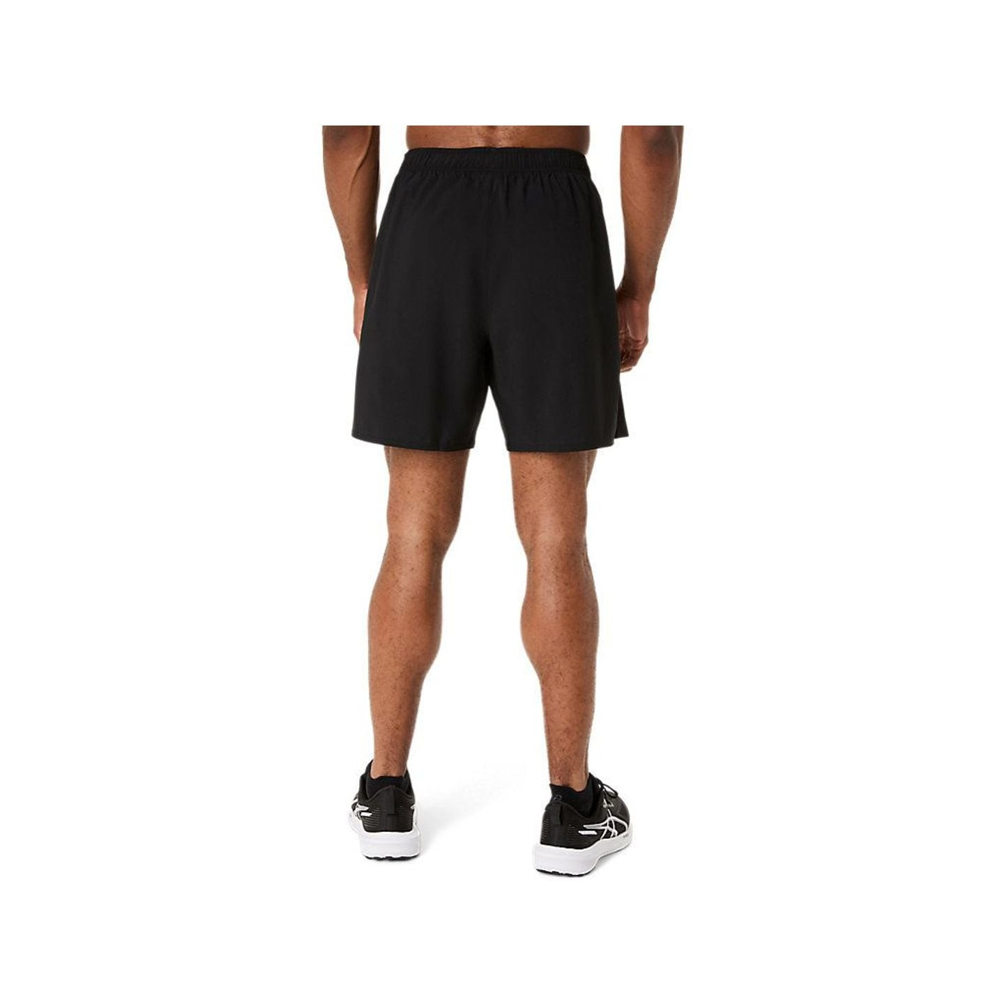 Athlète de dos portant le short de running ASICS ICON 7IN SHORT noir et des baskets noires sur fond 