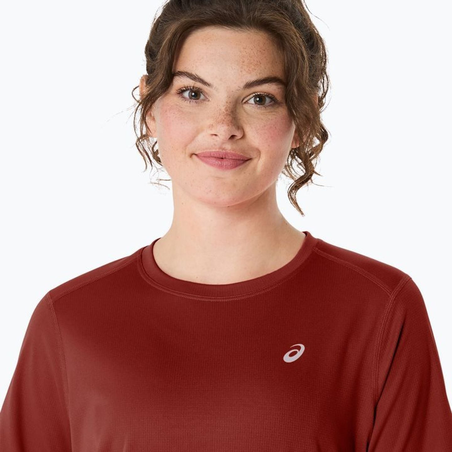 Portrait de face d'une femme portant le ASICS Core SS Top rouge rouille avec logo blanc sur la poitr