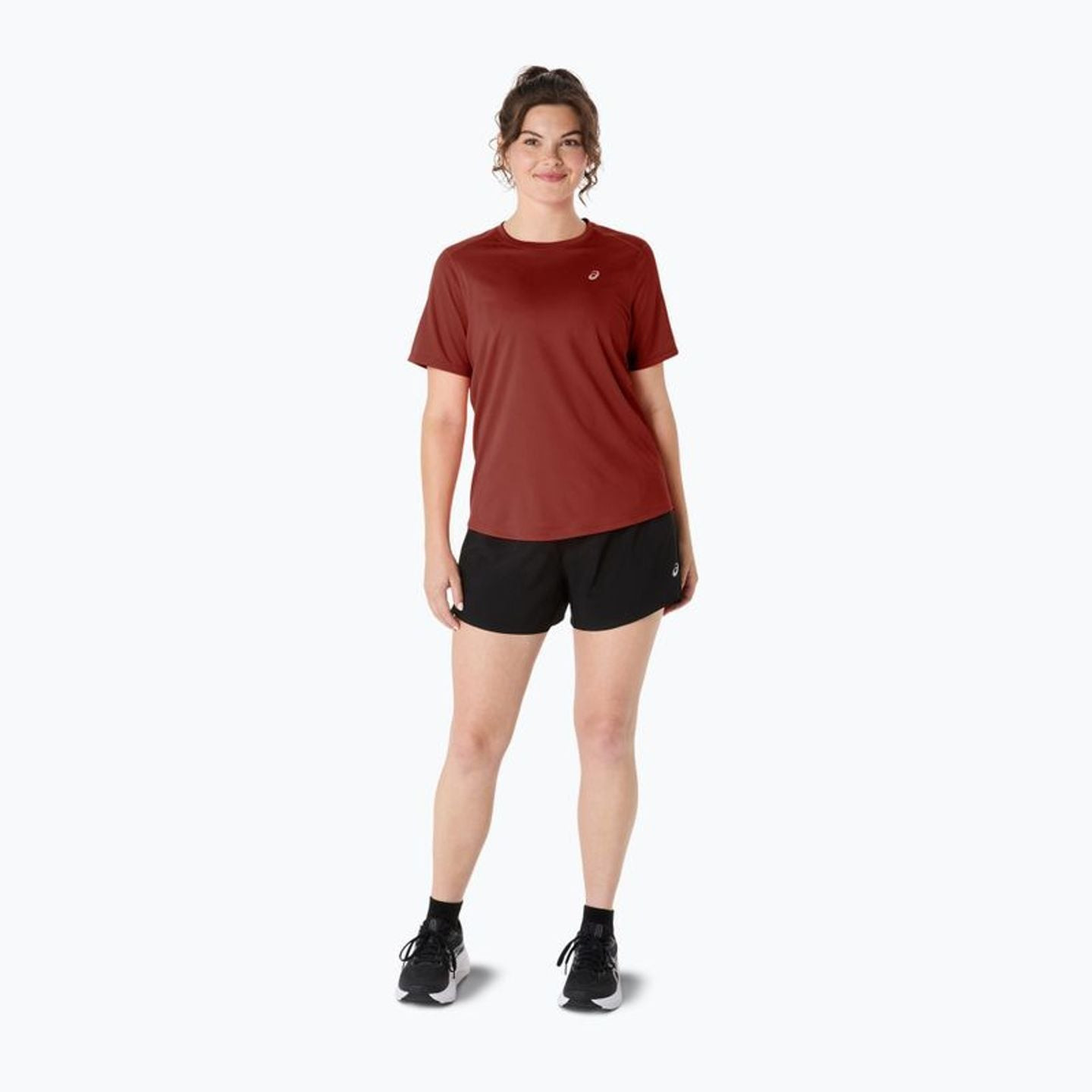 Vue en pied d'une coureuse portant le t-shirt ASICS Core SS Top rouge rouille, short noir et chaussu