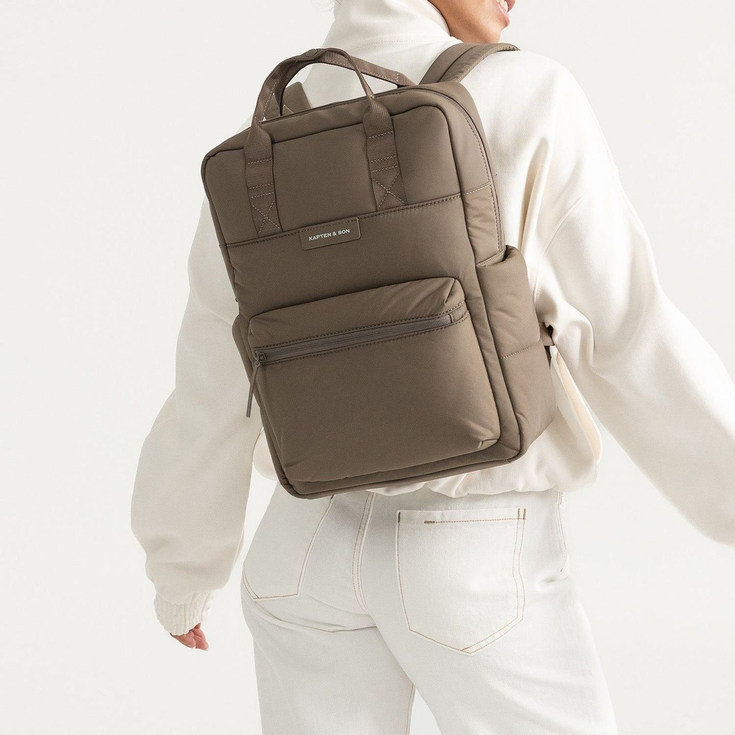 Personne en pull crème et jean blanc portant le sac à dos Bergen Cloud Walnut, montrant les bretelle