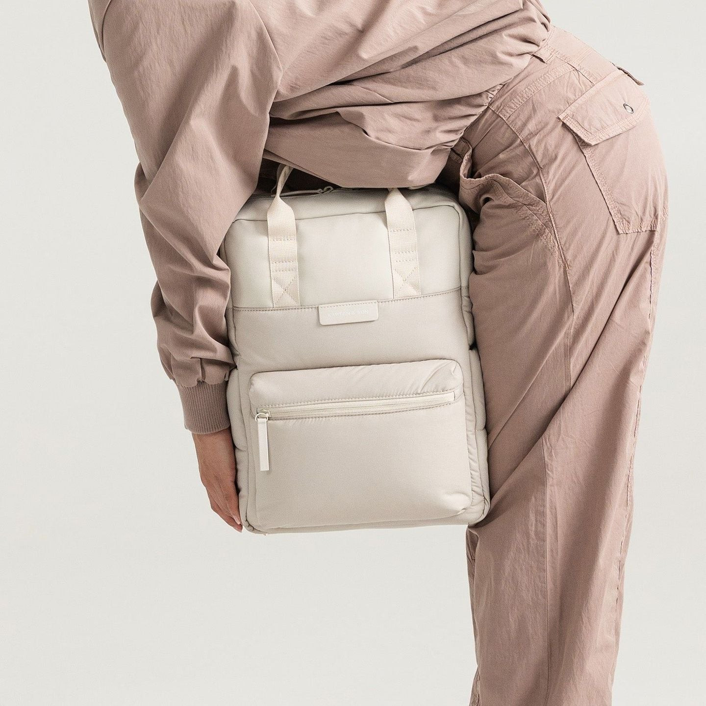 Personne en tenue beige portant le sac à dos Kapten & Son Bergen Cloud gris sable par sa poignée sup