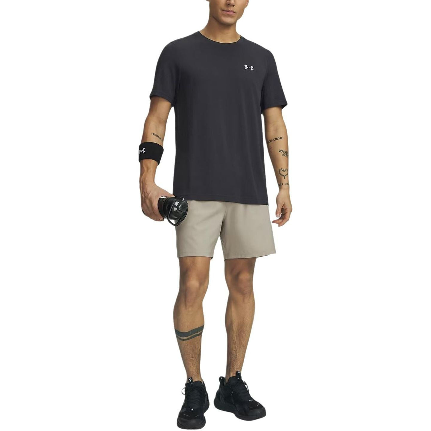 Homme portant le short UA Vanish Woven 2.0 6 pouces Timberwolf Taupe, t-shirt noir et casque audio a