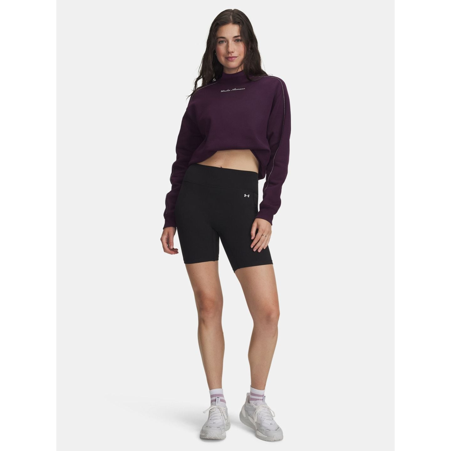 Photo lifestyle d'une femme en sweat court violet et short cycliste Under Armour Motion noir sur fon