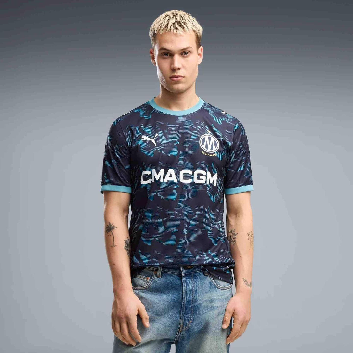 Mannequin portant le maillot extérieur réplique OM 2026/27 et un jean, vue de face sur fond studio g