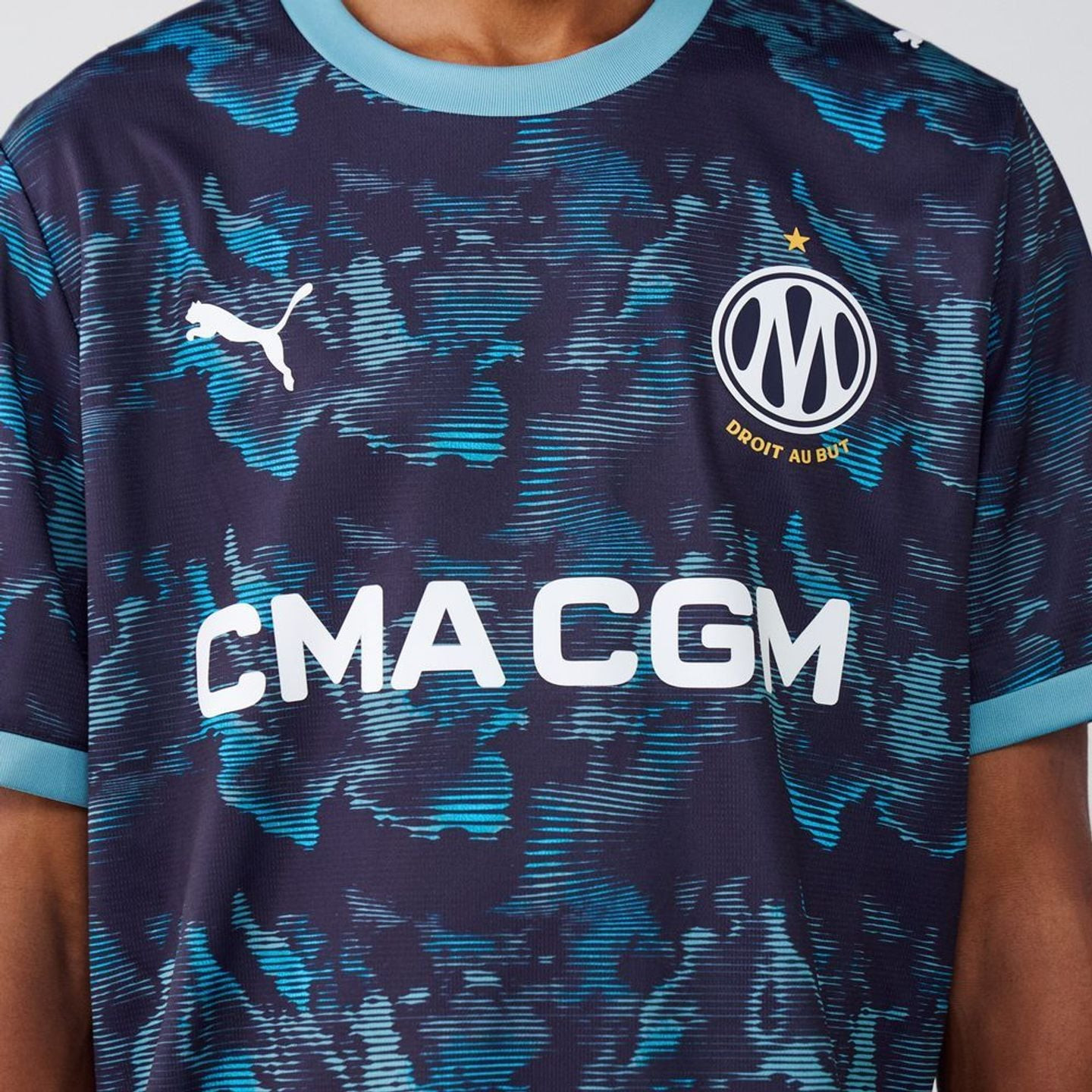 Gros plan sur le torse du maillot extérieur OM : logo PUMA, écusson OM, étoile dorée et sponsor CMA 