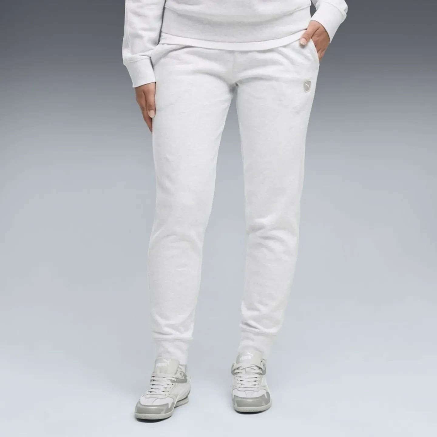 Mannequin portant un pantalon de survêtement Puma Elevated FL CL blanc avec baskets grises, mains da