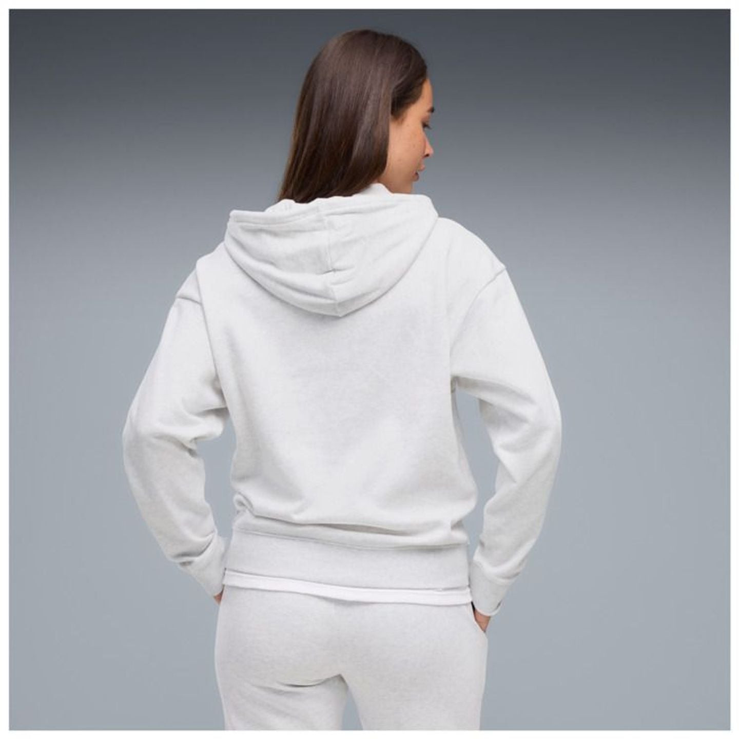 Femme vue de dos portant le sweat à capuche PUMA ESS Elevated Comfort Hoodie FL blanc et un jogging 