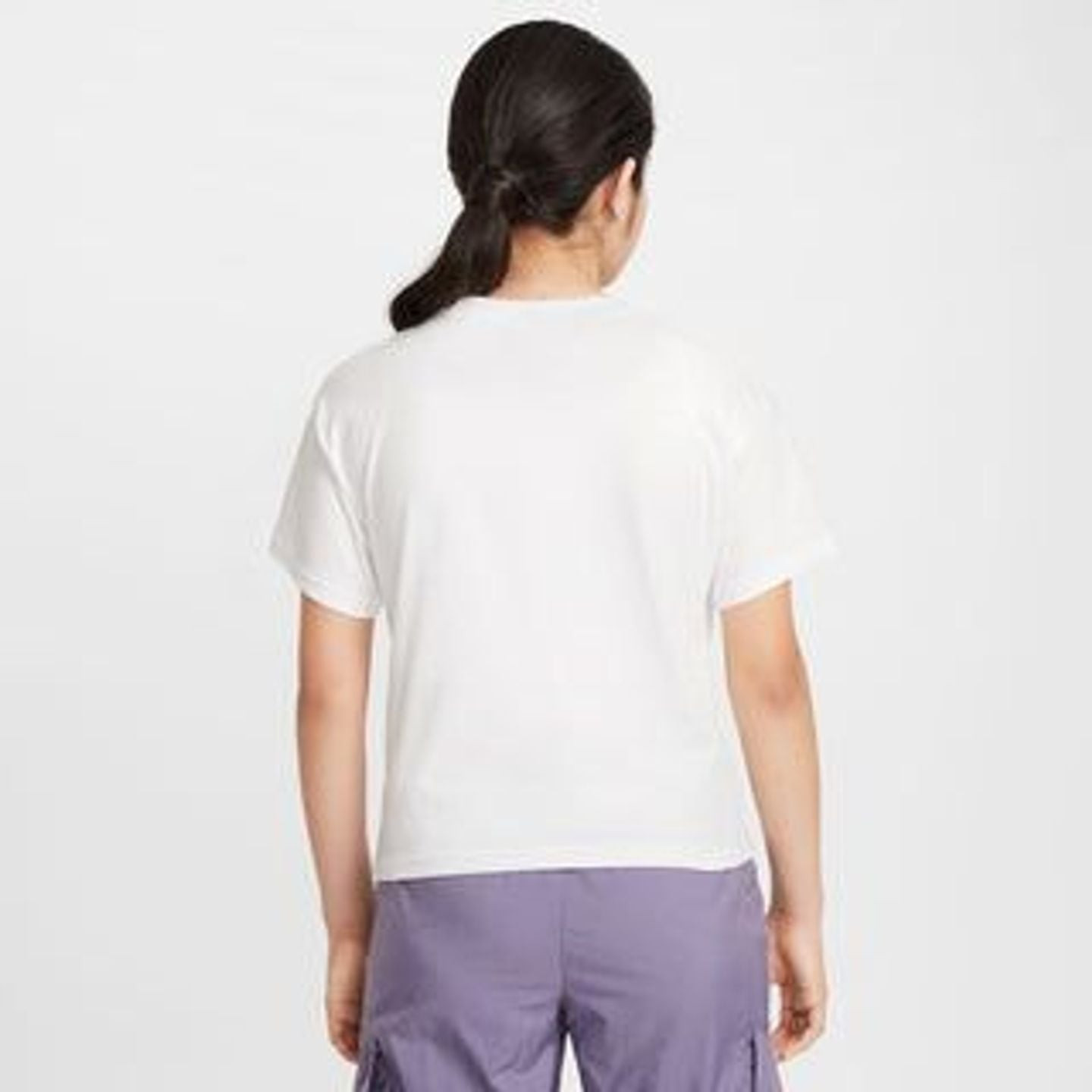 Jeune fille souriante portant le t-shirt Nike Sportswear Essential coupe boxy dans un cadre urbain.