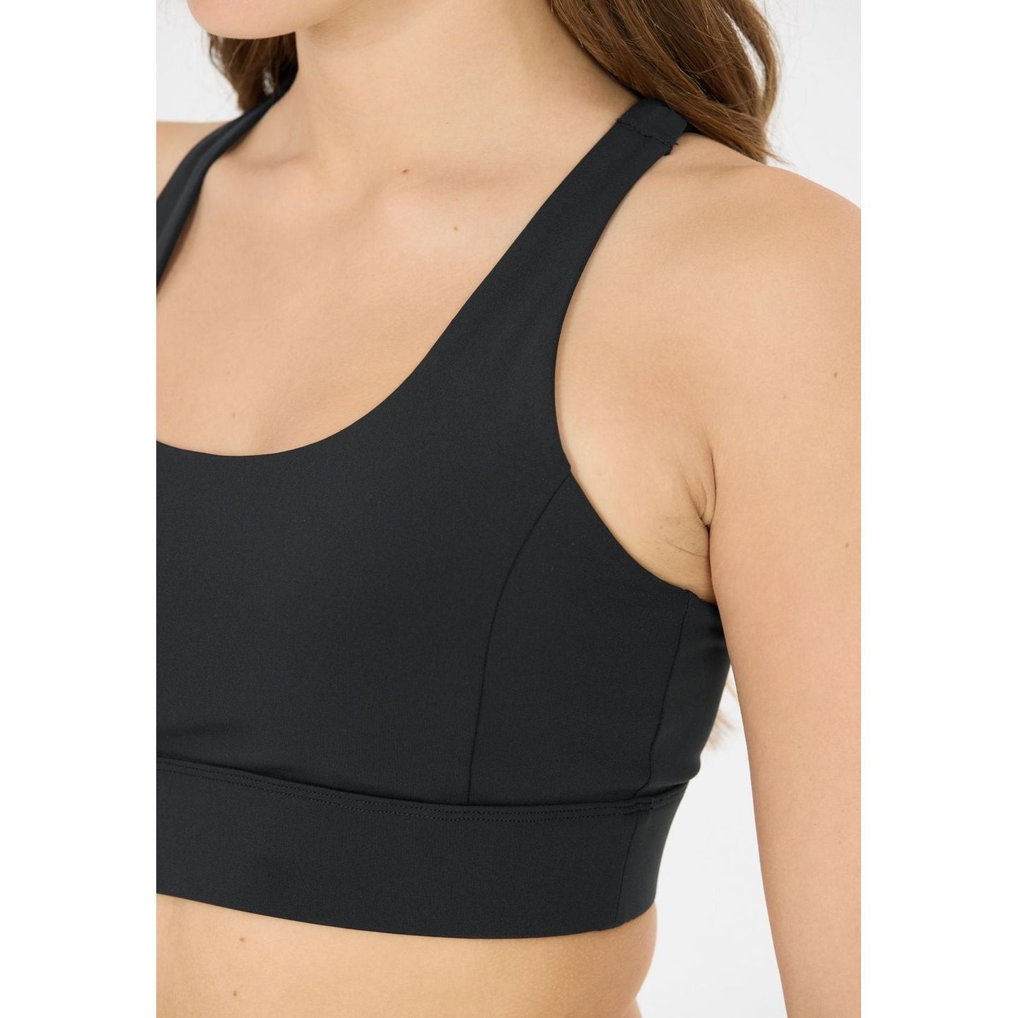 Gros plan latéral d’un mannequin portant la brassière Athlecia noire, large bretelle, panneau latéra