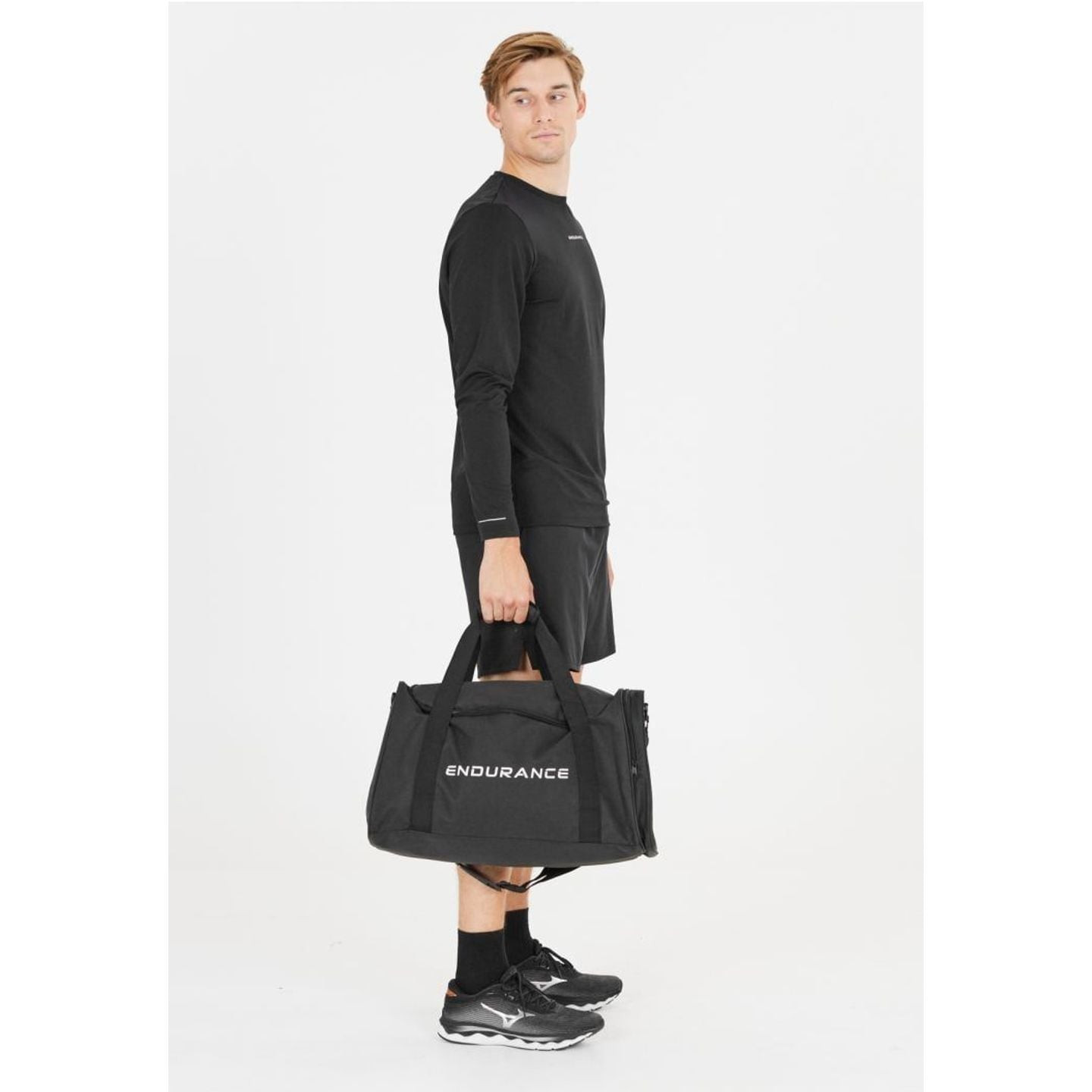 Homme tenant le sac de sport noir Endurance Lanakila 40 L par ses poignées, vue en pied