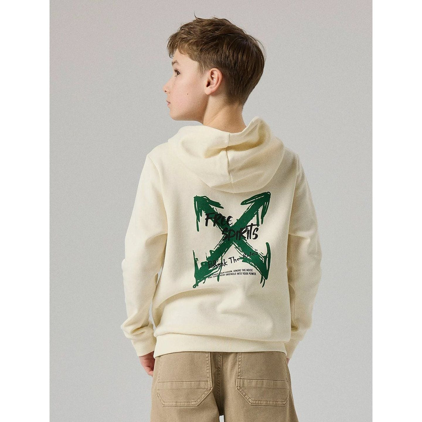 Garçon de dos portant un sweat à capuche crème avec grand X vert imprimé au dos