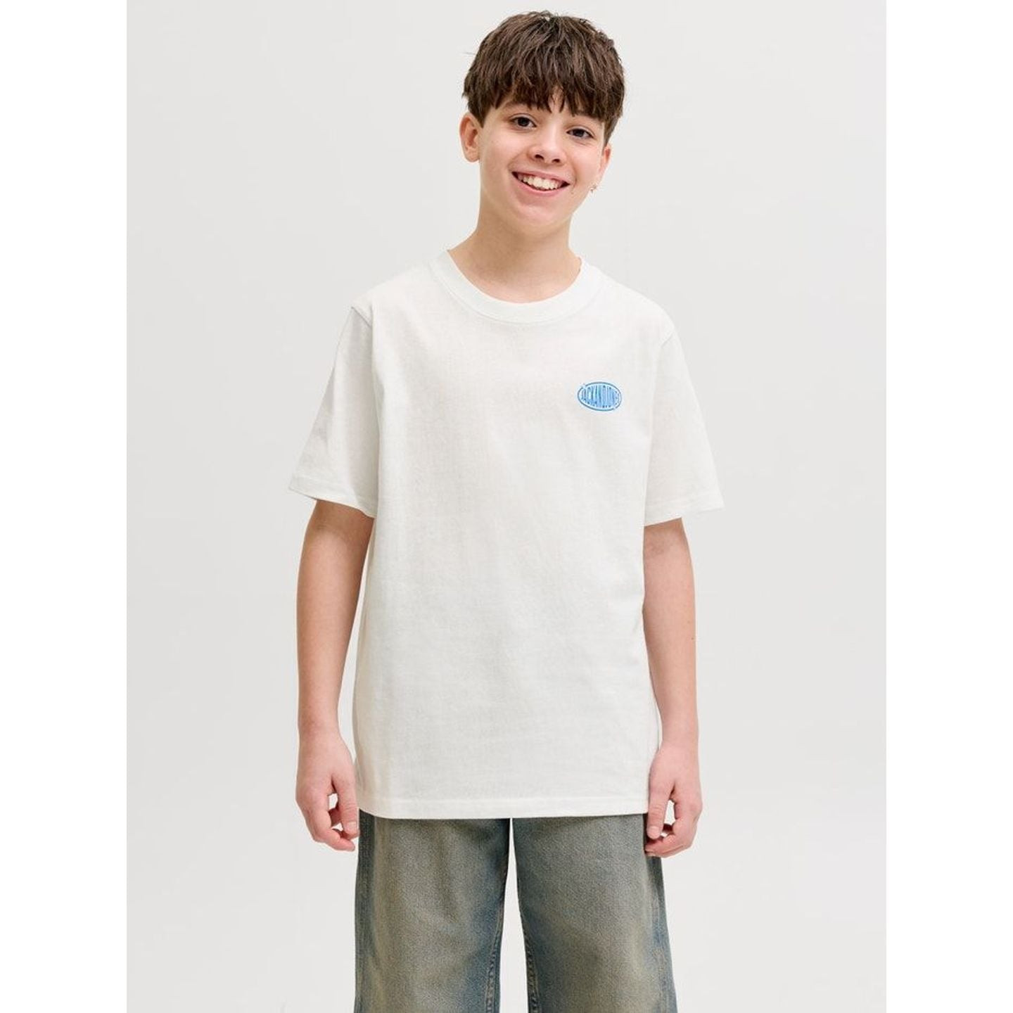 Garçon souriant portant le t-shirt col rond blanc JACK & JONES JUNIOR avec petit logo bleu sur la po