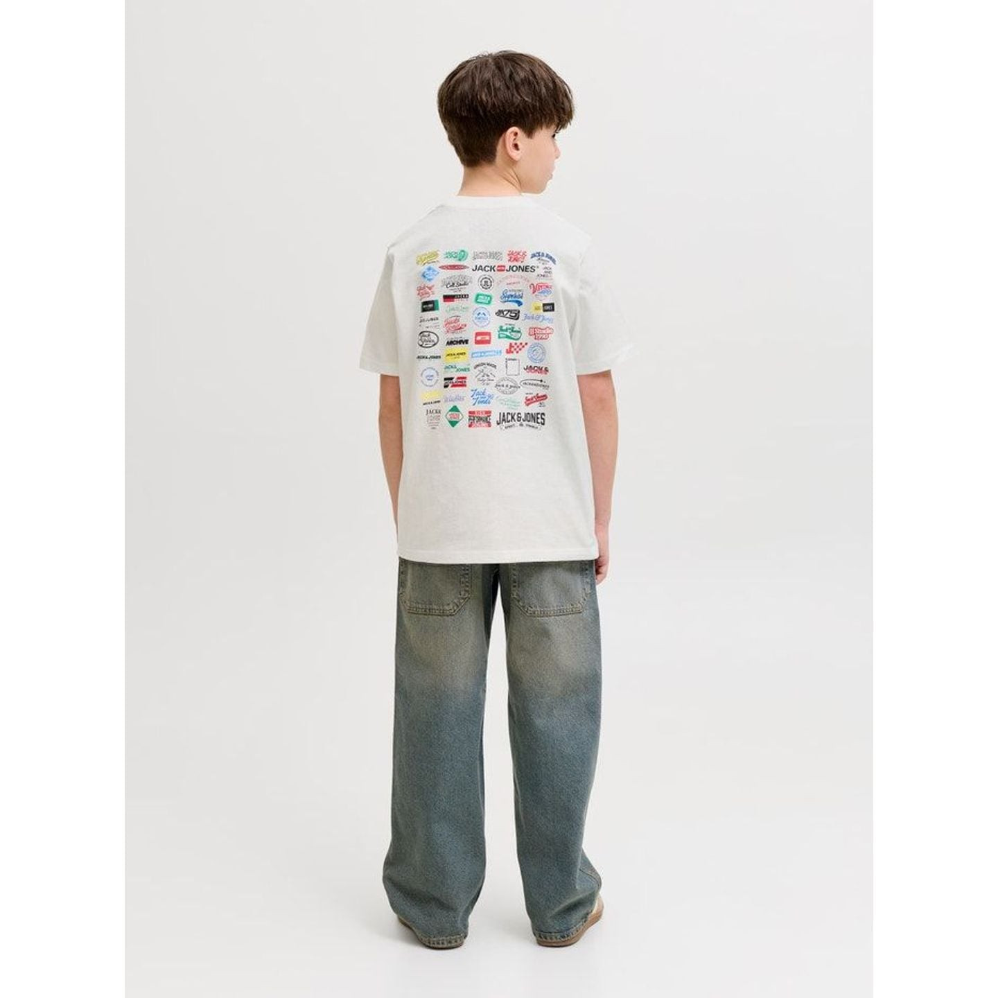 Vue de dos d'un garçon portant le t-shirt blanc JACK & JONES JUNIOR, imprimé collage de logos coloré