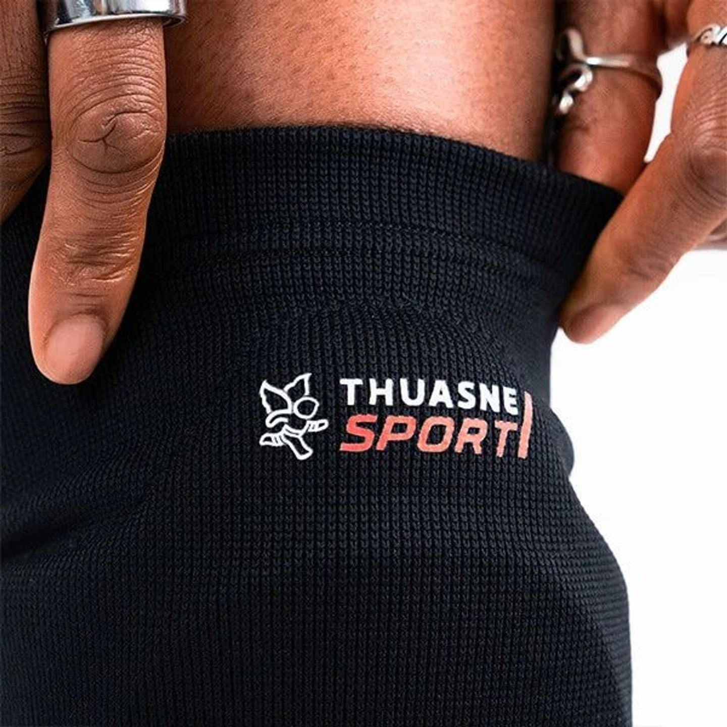 Gros plan sur le tricot noir de la genouillère Thuasne Sport volley, logo imprimé et mains sur le bo