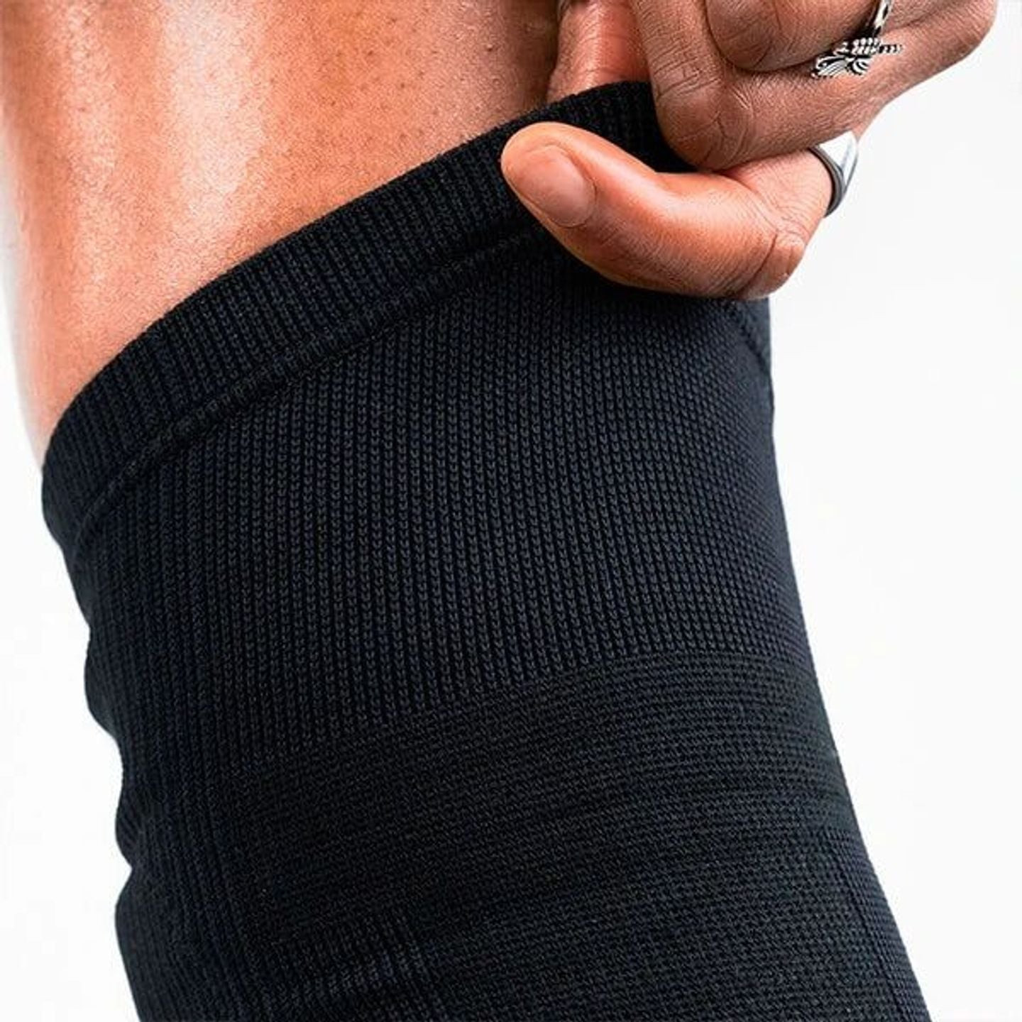 Gros plan sur le tricot côtelé noir d'une genouillère de volley Thuasne étiré par une main