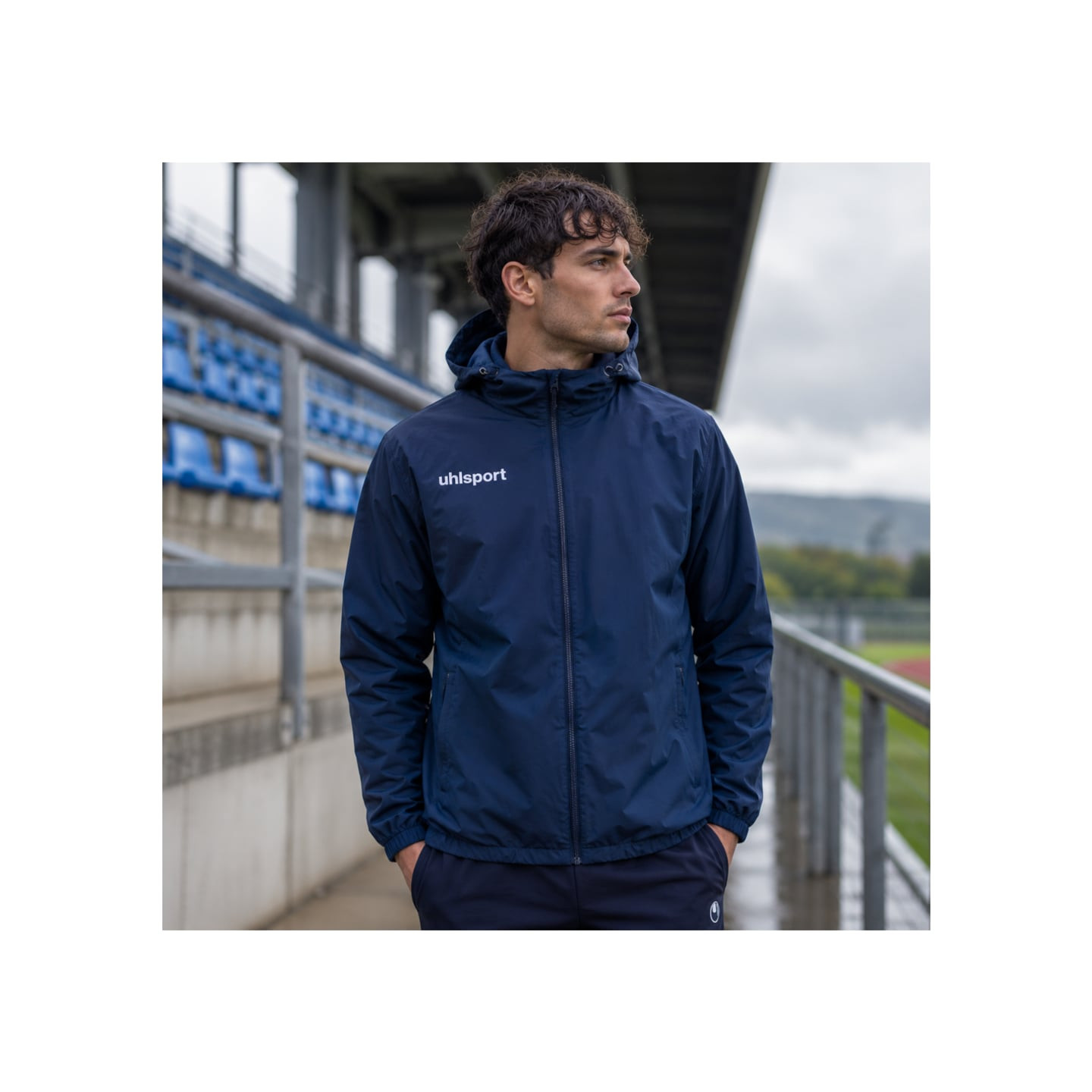 Un sportif porte la Uhlsport Veste De Pluie Essential Doublée Polaire Imperméable Unisexe sous une a