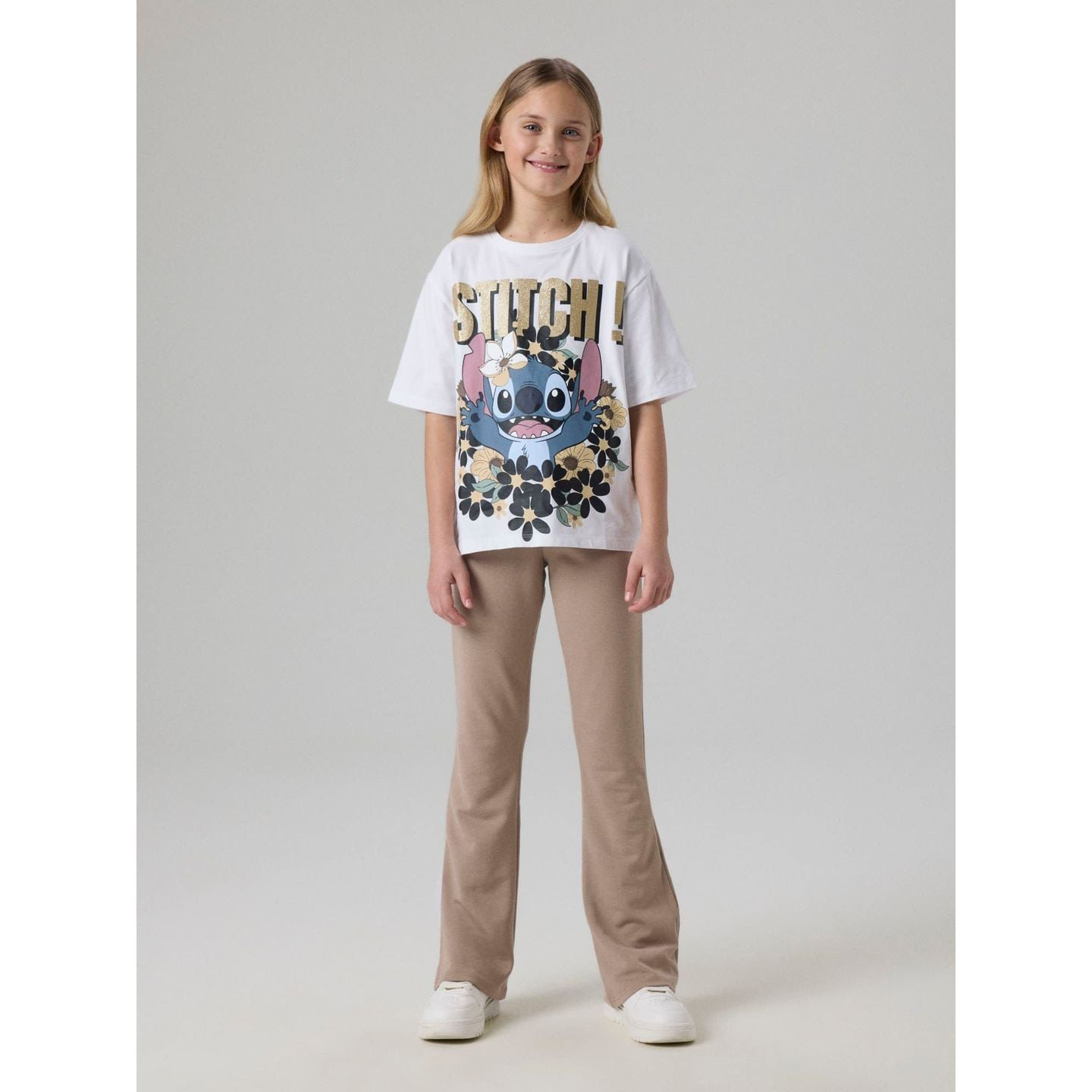 Fille portant le t-shirt Stitch blanc avec imprimé doré à paillettes, associé à un pantalon beige et