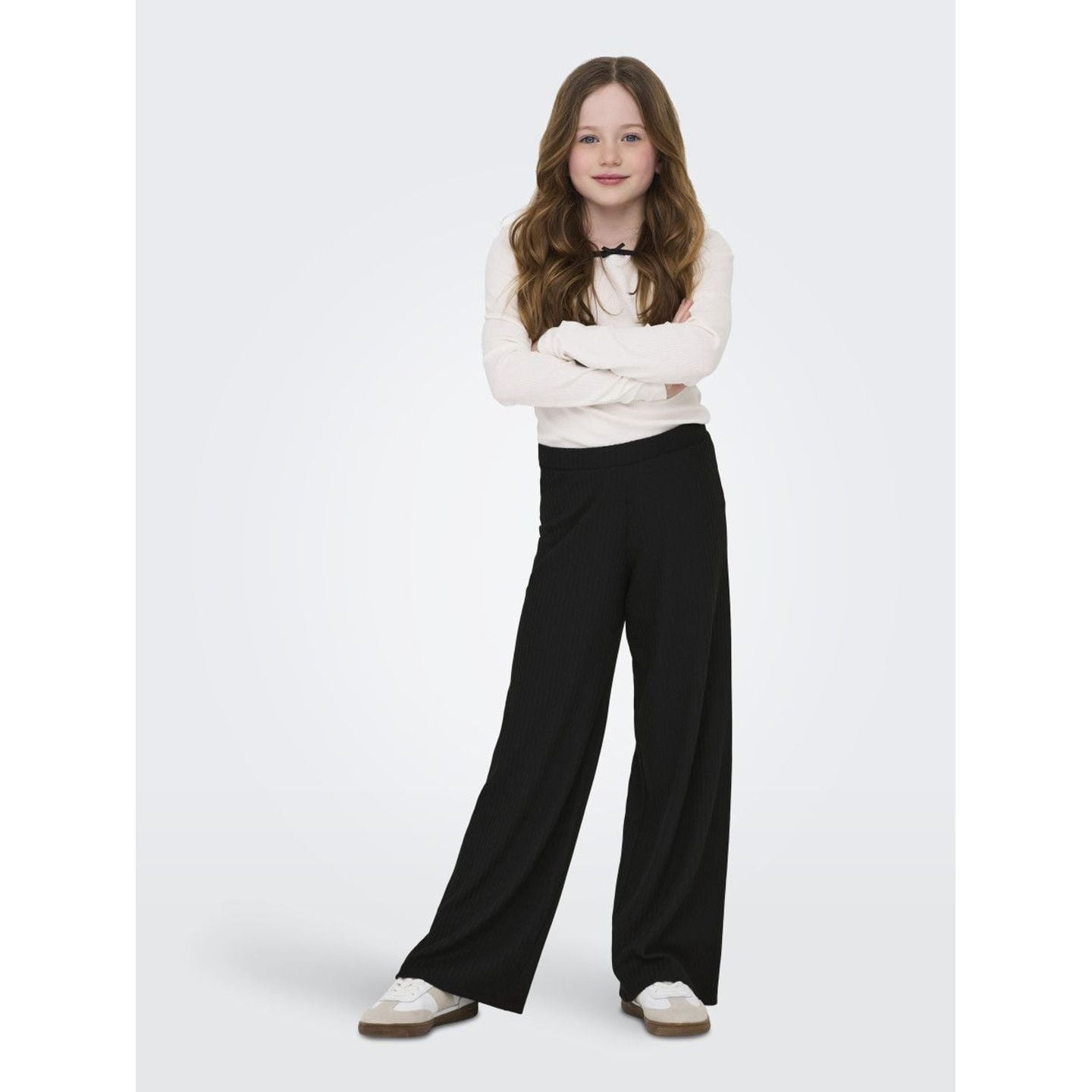Fille debout, bras croisés, portant le pantalon large noir KOGNELLA PANT JRS NOOS et un haut blanc