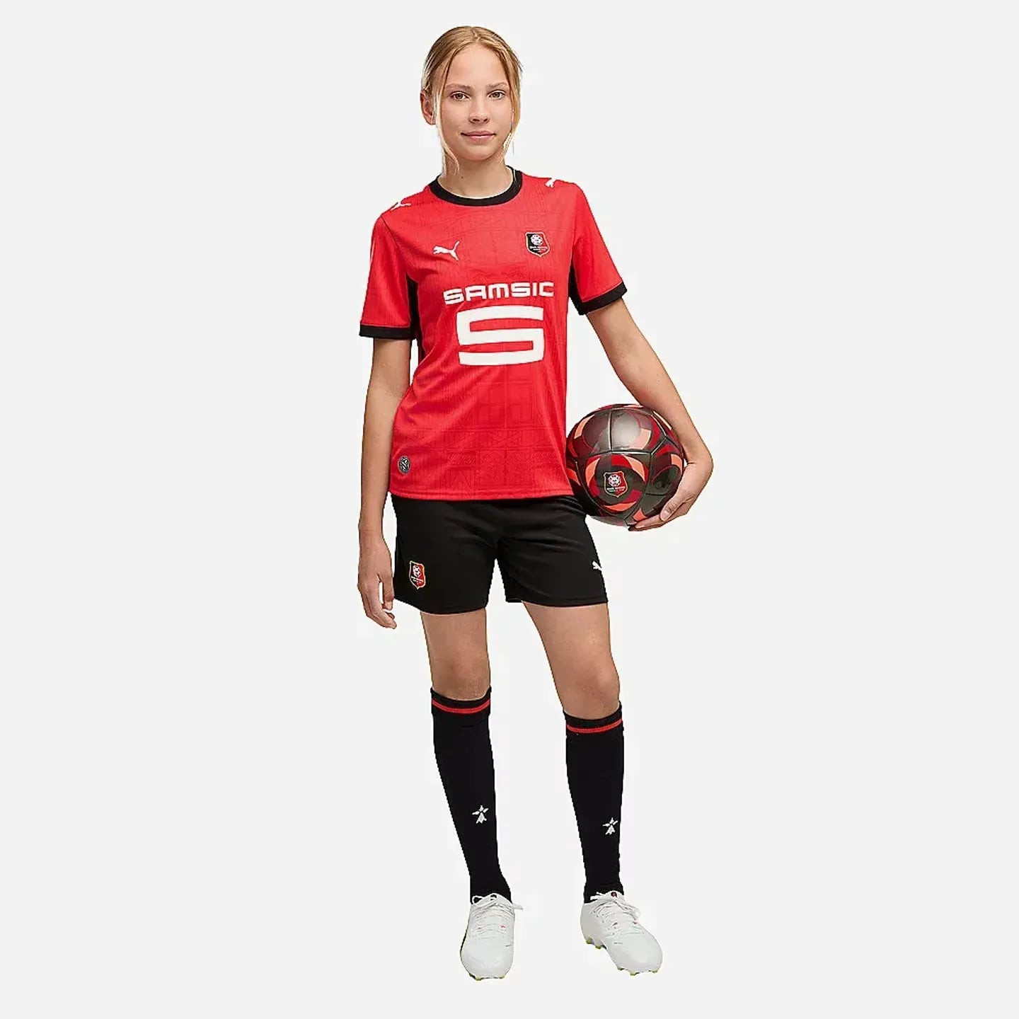 Jeune footballeuse en maillot rouge du SRFC et short Replica Jr noir, tenant un ballon, vue studio e