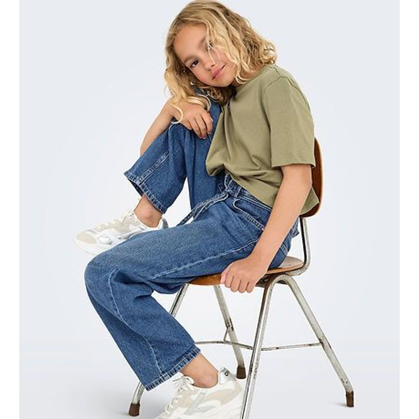 Fille assise sur une chaise portant un jean droit KOGGIANNA bleu, un t-shirt vert olive et des baske