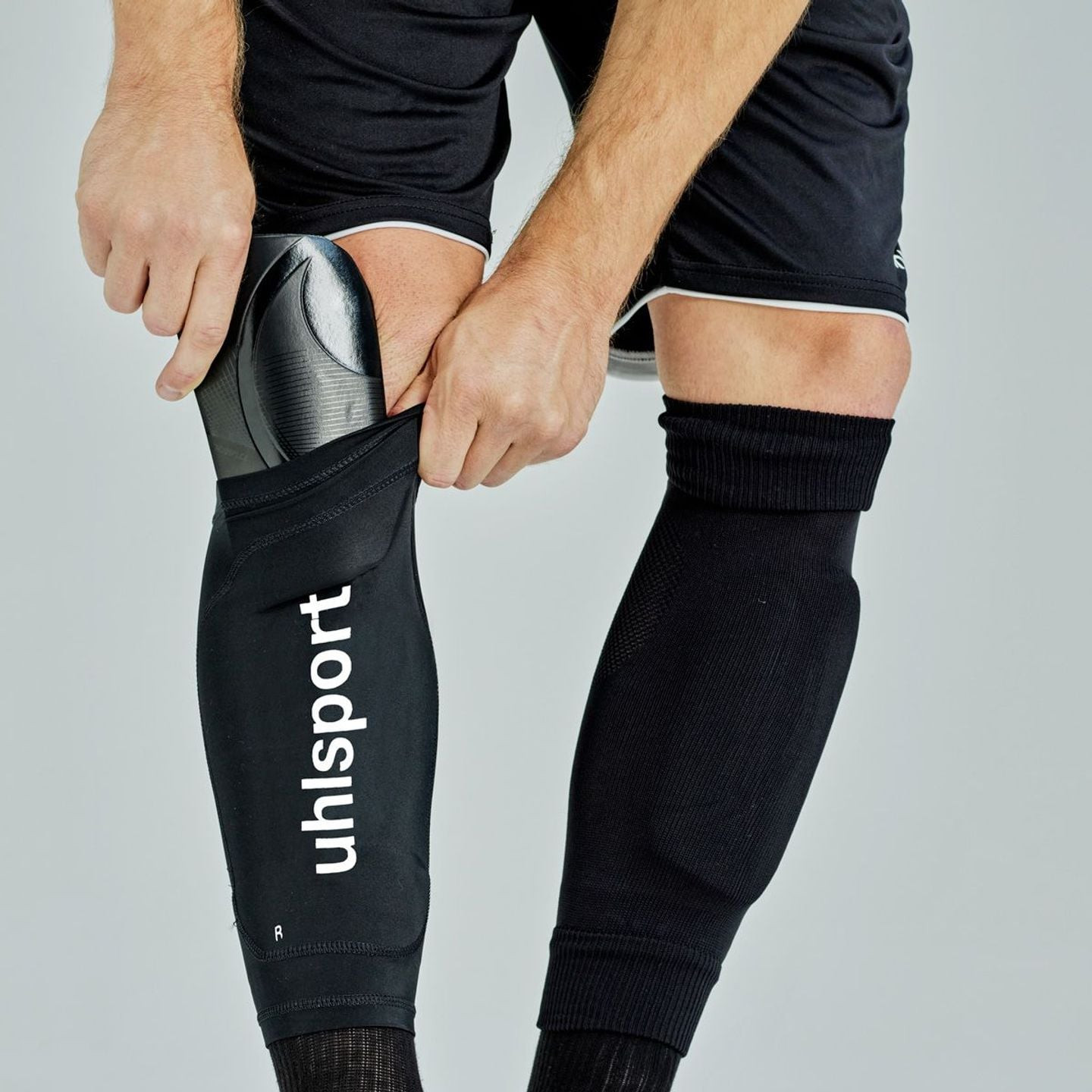 Joueur de football glissant un protège-tibia dans la poche d'un manchon Uhlsport noir porté sur le m