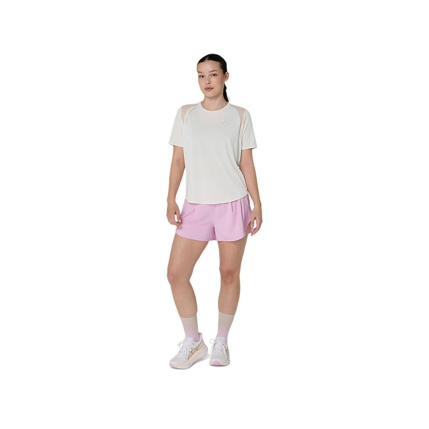 Vue en pied d'une femme portant un short de running ASICS ROAD 3.5IN rose et un haut blanc, prête à 
